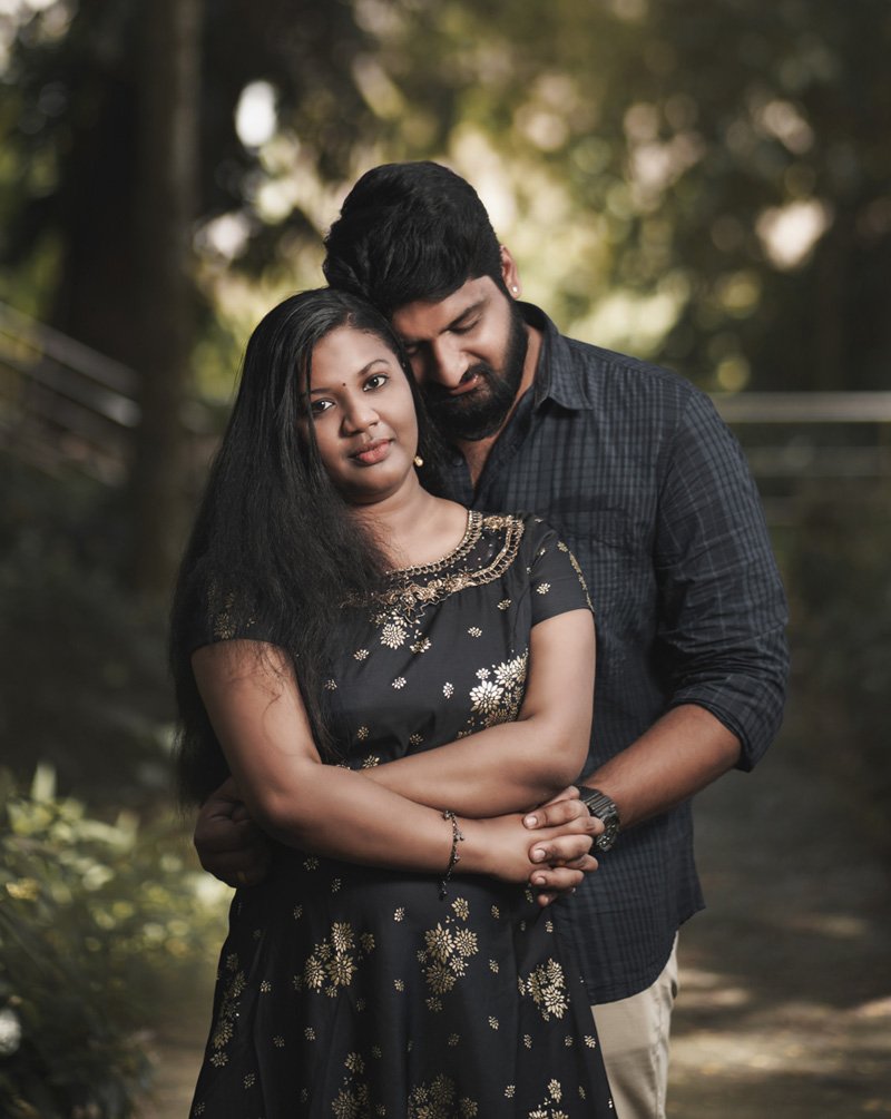 Couple embracing outdoors under trees, the woman in a black dress with gold embroidery