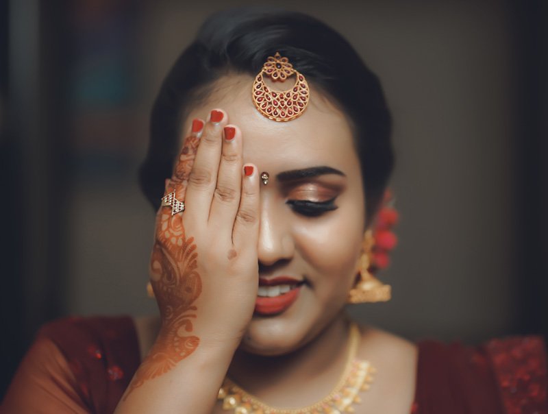 Bride with henna on her hand covering one eye, wearing a gold hair ornament