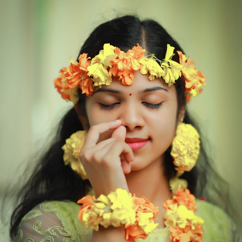 Young woman with a crown and garlands of orange and yellow flowers, eyes closed