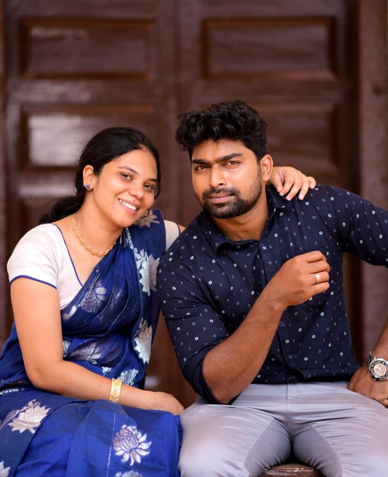 Smiling couple sitting in front of a wooden door, the woman in a blue saree