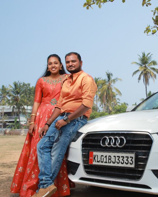 Couple standing beside a white car, the woman in an orange dress and the man in an orange shirt